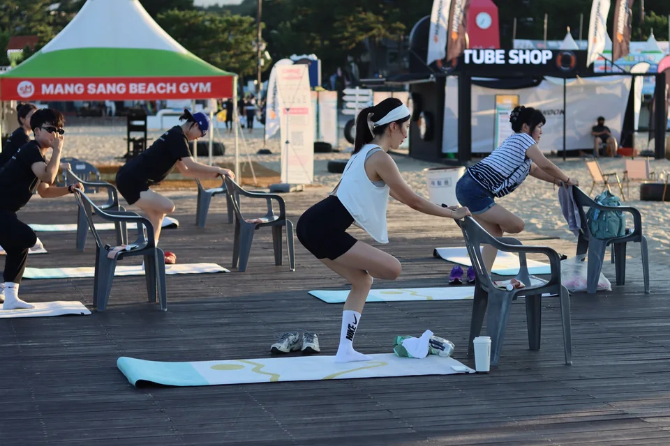해변 데크에서 의자를 잡고 함께 동작을 따라 하는 그룹 클래스 참가자들
